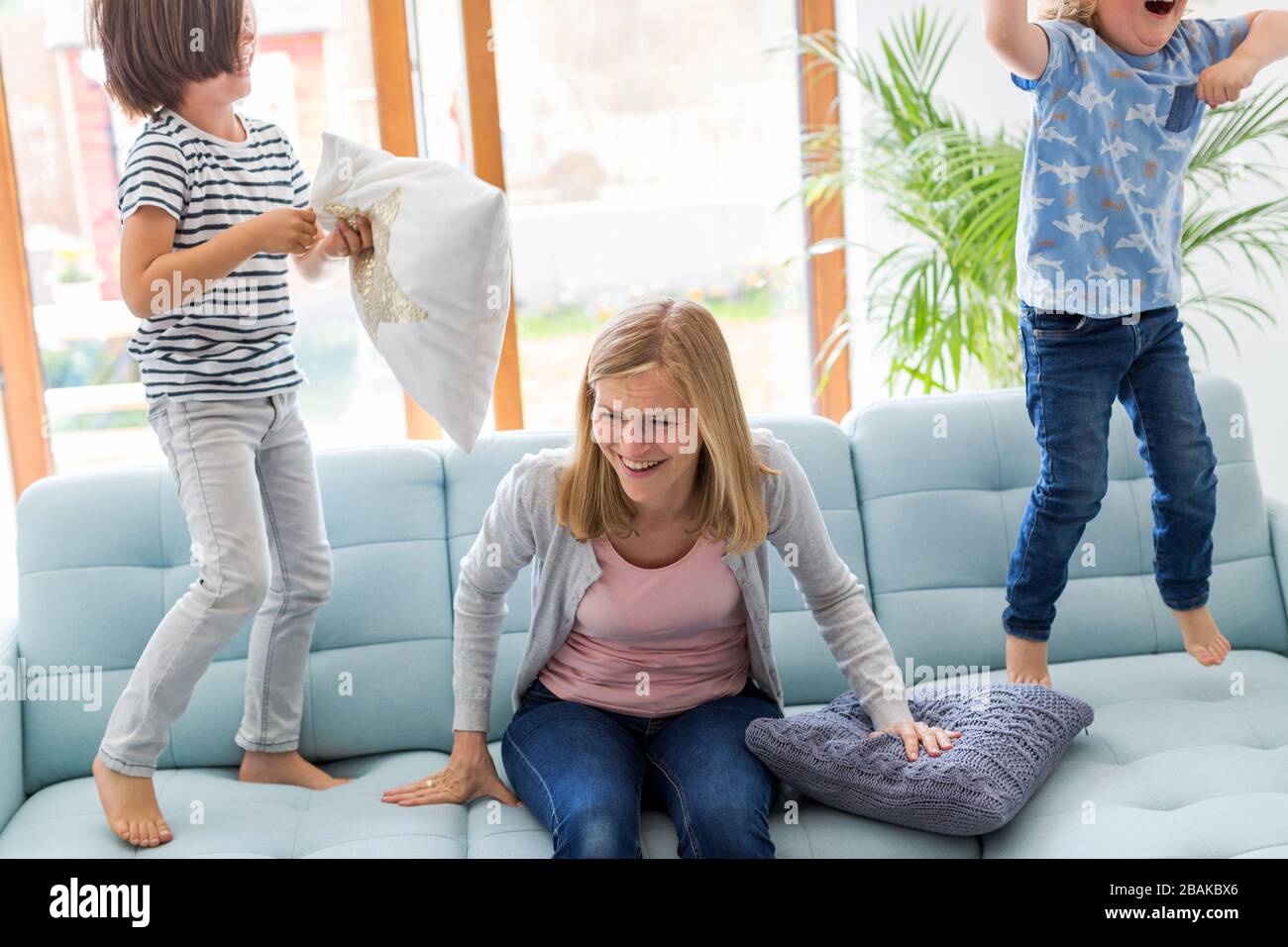 Mutter mit Kopfschmerzen und Kinder springen auf dem Sofa Stockfoto