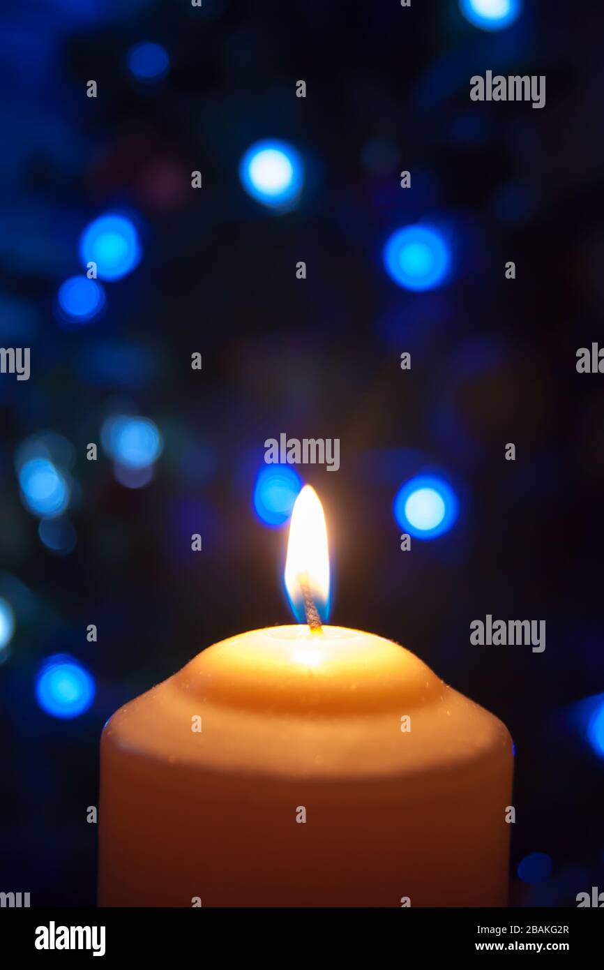 Eine große Kerze brennt vor dem Hintergrund einer Girlande mit strahlendem Licht. Vertikales Foto, Unschärfe. Mystische esoterische Romantik Divination Stimmung getauft Weihnachts-Karol-Setcer Stockfoto