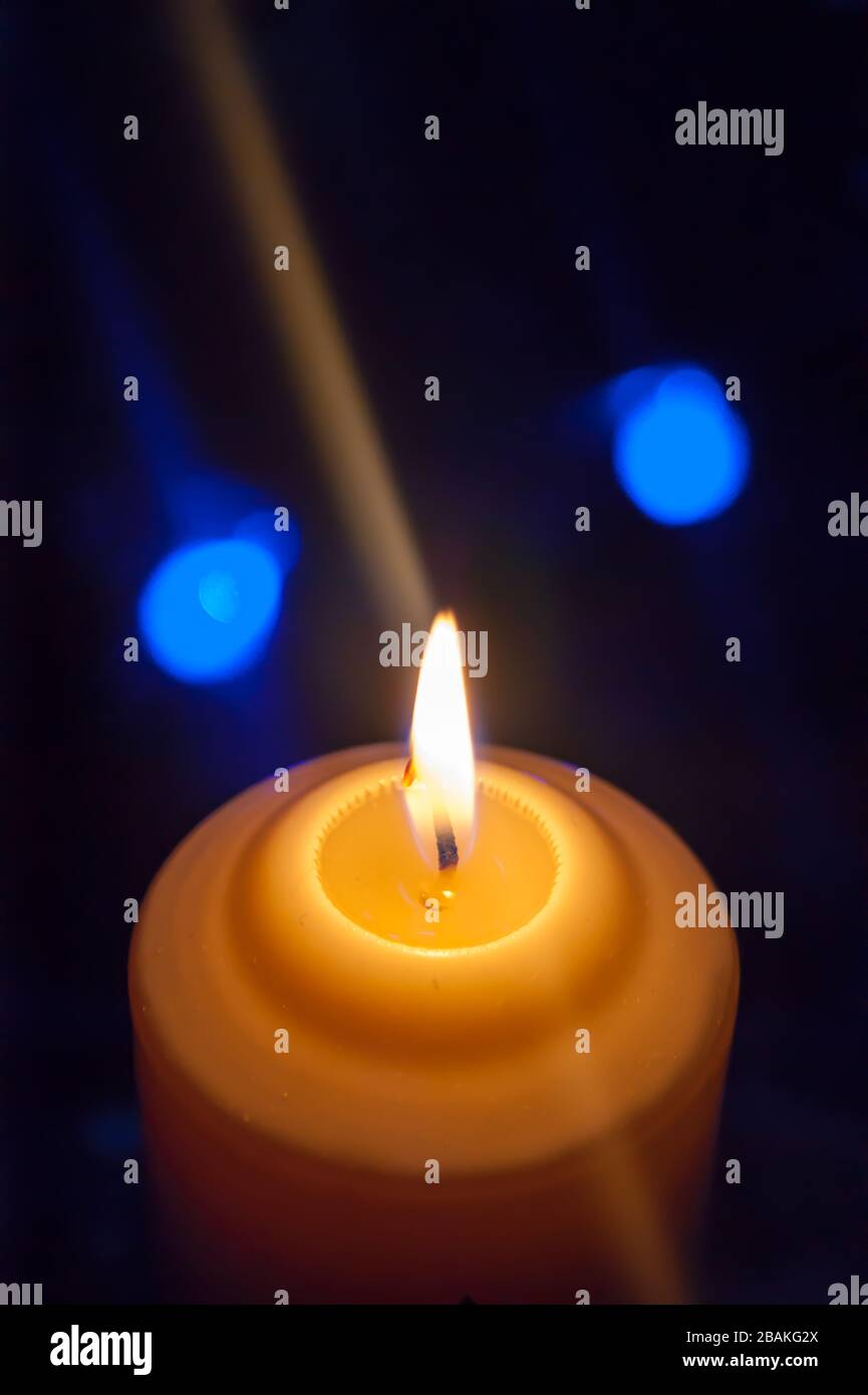 Eine große Kerze brennt vor dem Hintergrund einer Girlande mit strahlendem Licht. Vertikales Foto, Unschärfe. Mystische esoterische Romantik Divination Stimmung getauft Weihnachts-Karol-Setcer Stockfoto