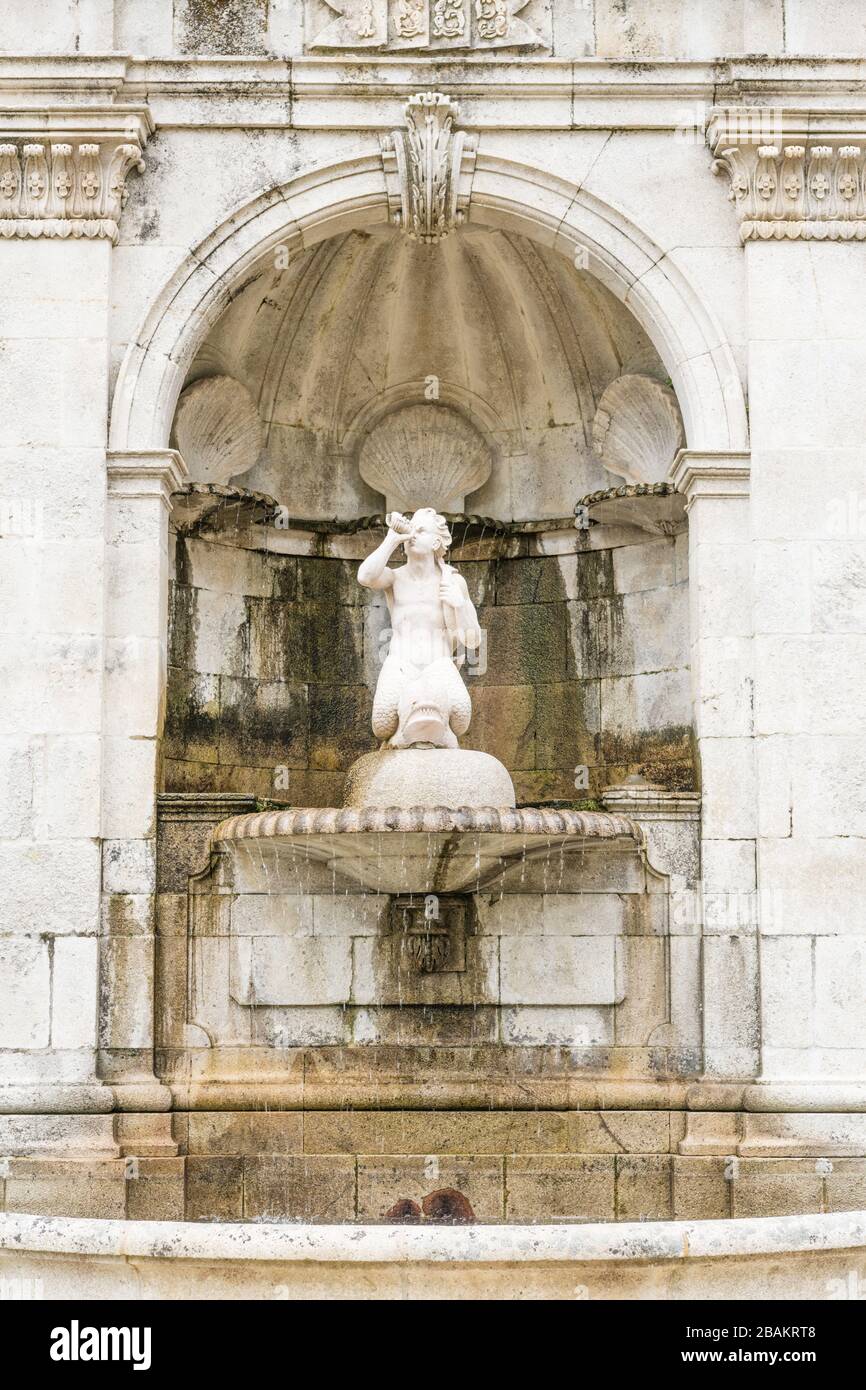 Alter Wasserbrunnen in einer weißen Steinmauer mit Statue und verzierter Schalenornamentik in Lamego, Portugal Stockfoto