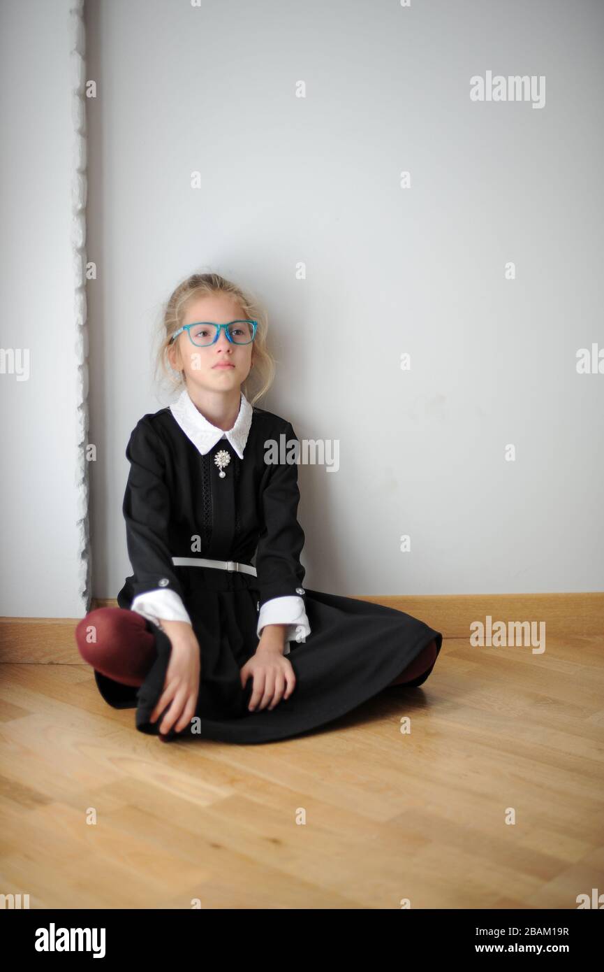 Verärgert weinendes kleines Mädchen in schwarz-weißem Kleid, das zu Hause auf dem Boden sitzt und sich an die Wand lehnt Stockfoto
