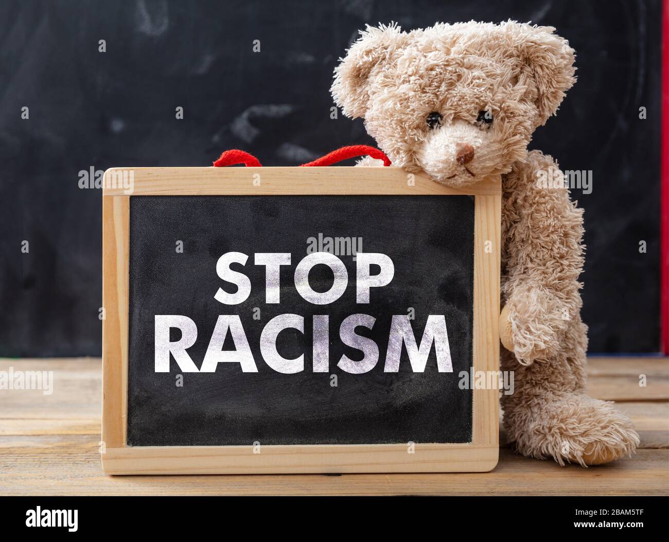 Halten Sie das Konzept von Rassismus und Kindern ein. Teddybär und ein Brett mit Stop Racism Text, Schulklasse Blackboard Hintergrund. Nein zur Botschaft des Rassismus für Kinder. Stockfoto