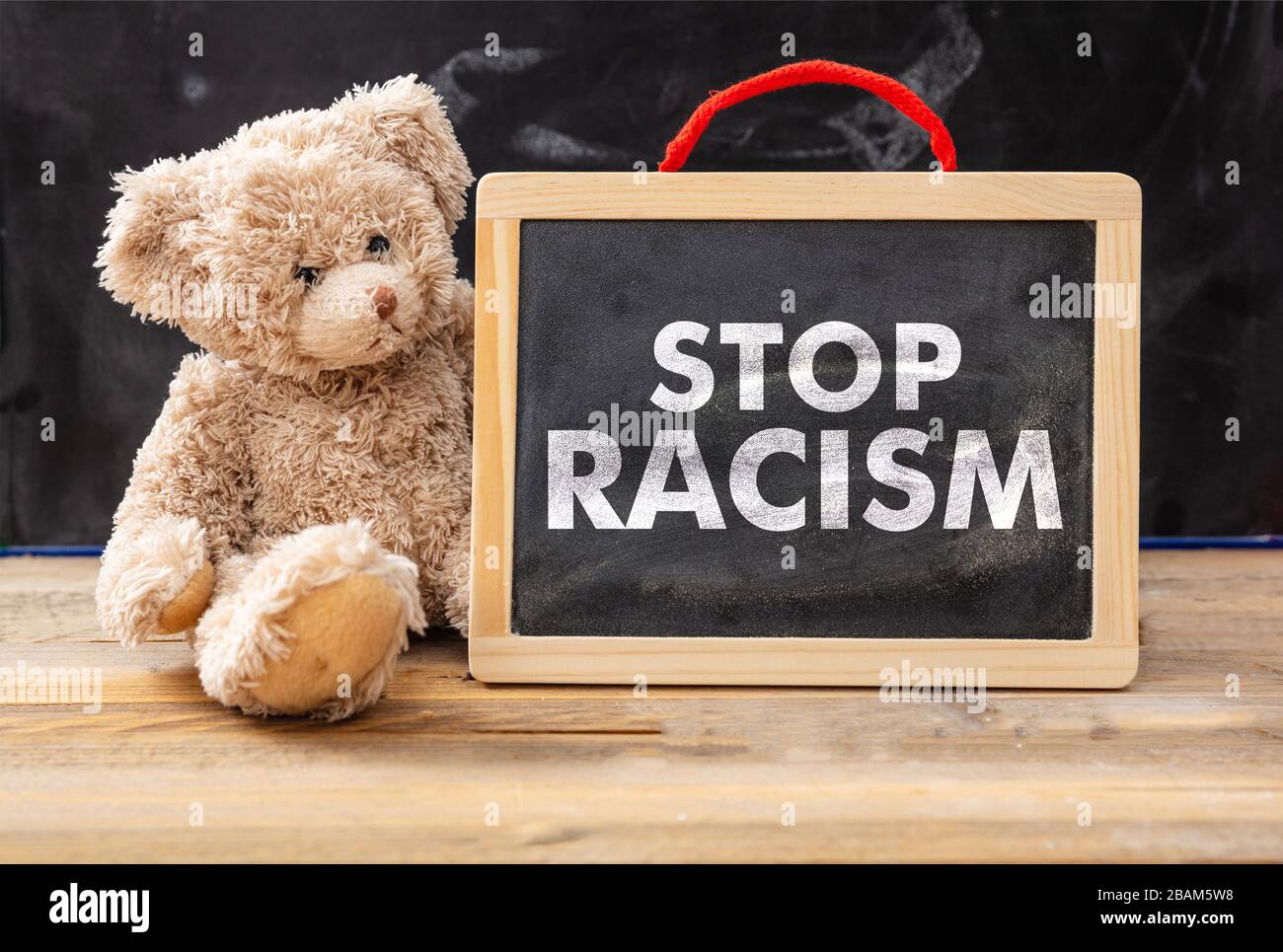 Halten Sie das Konzept von Rassismus und Kindern ein. Teddybär und ein Brett mit Stop Racism Text, Schulklasse Blackboard Hintergrund. Nein zur Botschaft des Rassismus für Kinder. Stockfoto