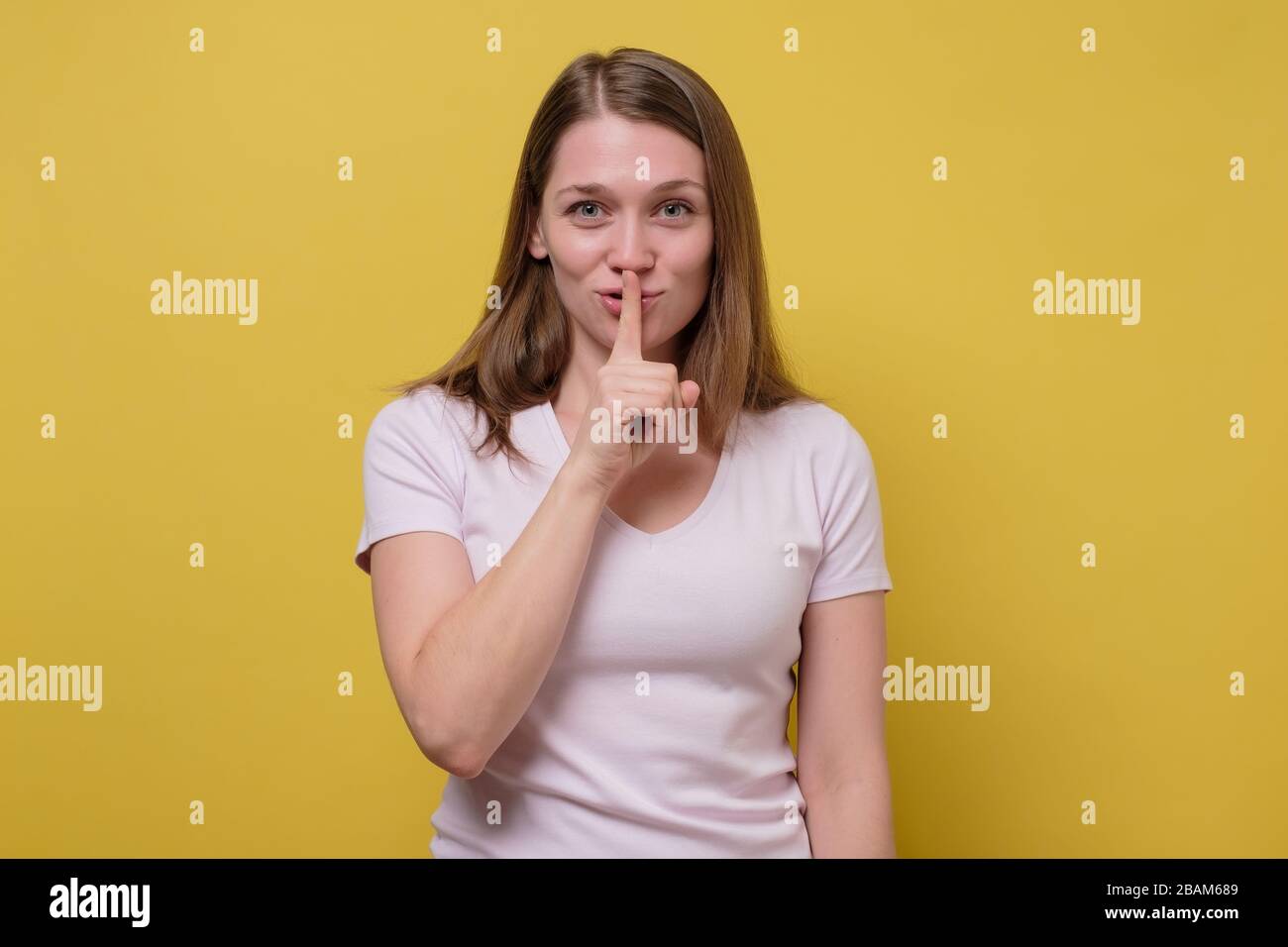 Schöne junge kaukasische Frau mit dem Finger an den Lippen fragen Sie sei leise, ein tausendjähriger weiblicher Blick auf die Kamera kündigt geheimen Verkauf oder Rabatt an. Studio Sho Stockfoto