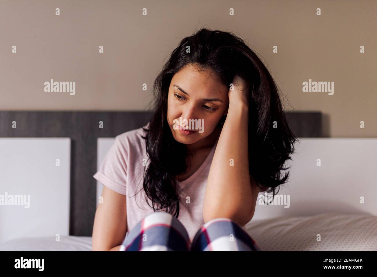 Traurige junge Frau, die allein im Bett in einem Zimmer sitzt. Konzept dramatischer Einsamkeit, Traurigkeit, Depression, traurig. Stockfoto