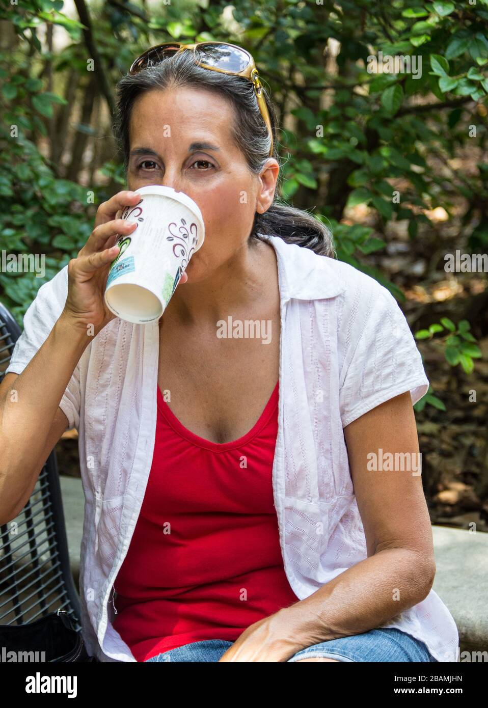 Frau mittleren Alters trinkt Kaffee in einem Park. Stockfoto