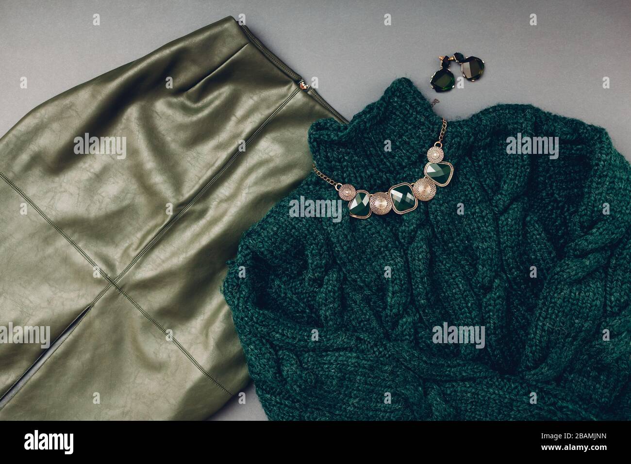 Modisches Outfit für Frauen. Modischer grüner Lederrock, Pullover, Schmuck. Accessoires für weibliche Federkleidung. Stockfoto