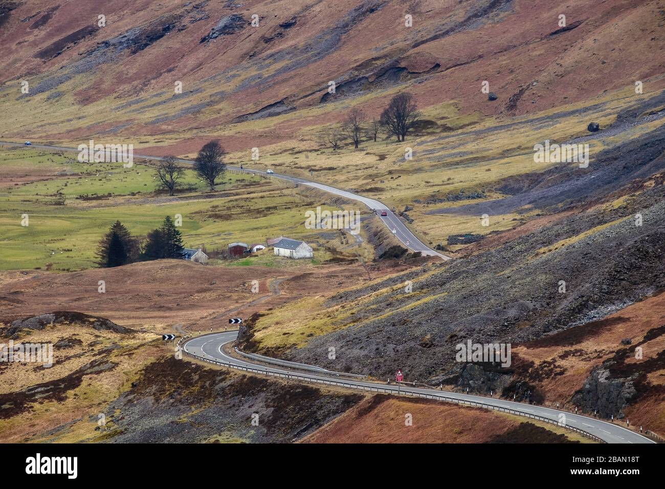 Eine Straße, die durch ein Bergtal der schottischen Highlands führt und ein weißes Haus. Glen Coe, Schottland Stockfoto