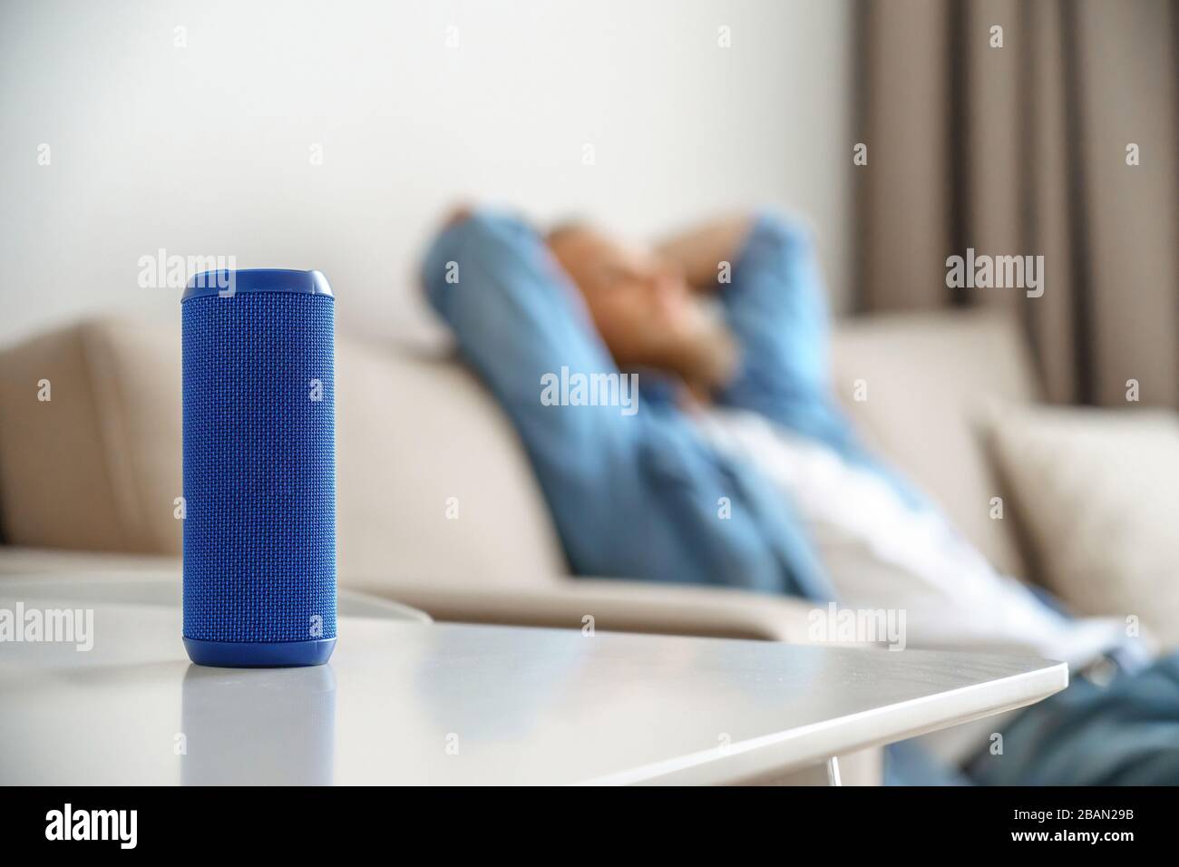 Kleiner tragbarer Lautsprecher auf dem Tisch mit Mann Lounge, der Musik zu Hause hört. Stockfoto