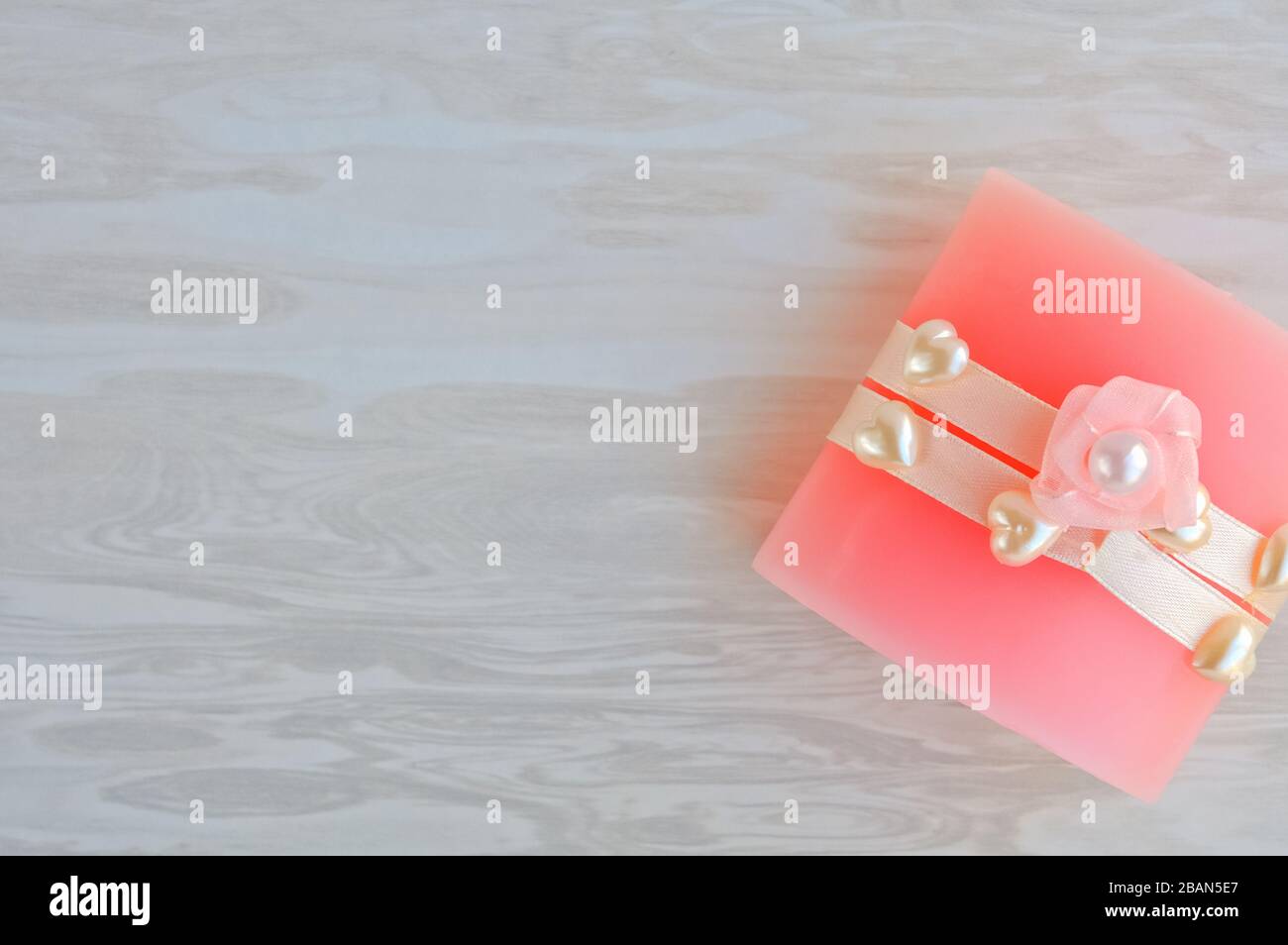 Rosa aromatische Kerze mit Herzen und einer Blume für ein Geschenk oder Glückwünsche auf einem Urlaub auf einem grauen Holzhintergrund mit Kopierraum dekoriert Stockfoto