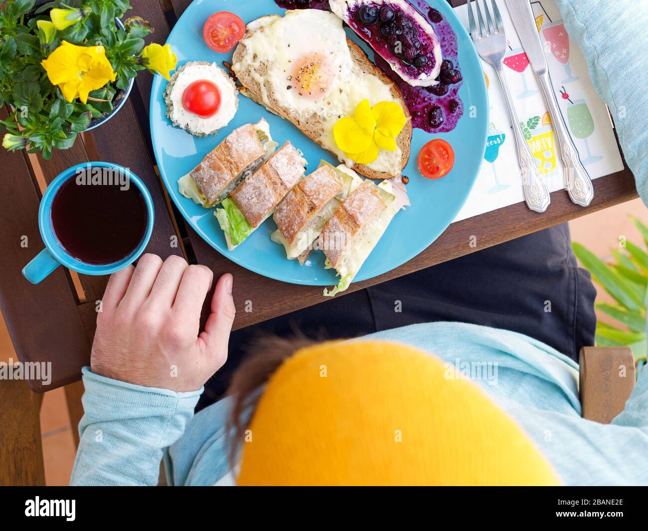 Wunderschönes, farbenfrohes Frühlingsfrühstück mit verschiedenen Speisen auf einem Holztisch mit Blumen und Händen, Blick von oben. Stockfoto