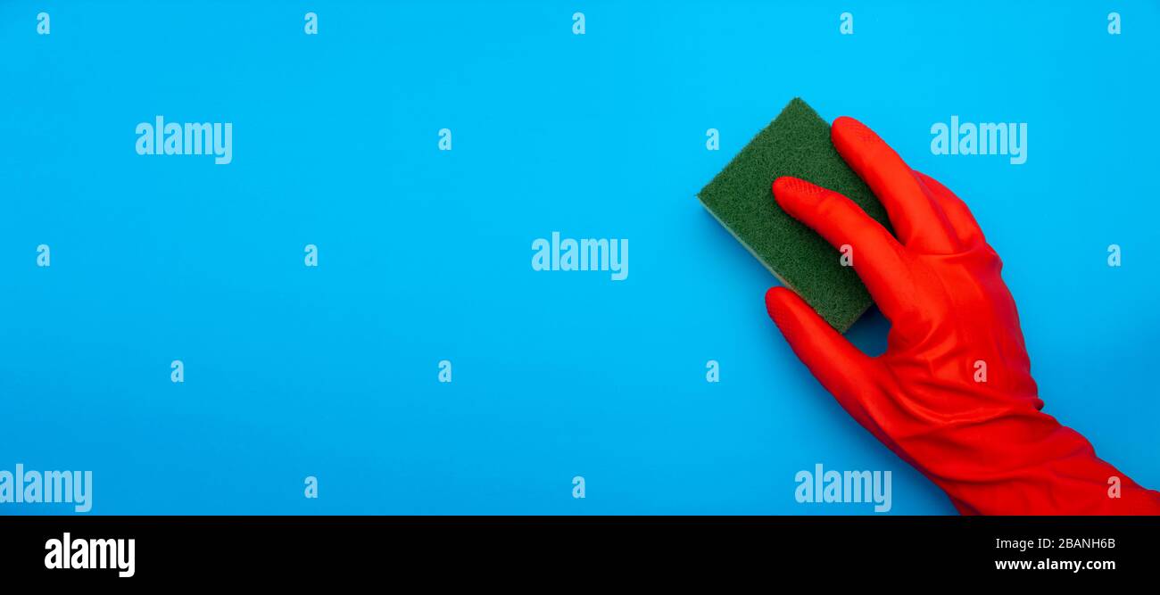 Konzeptbild der Hand aus rotem Gummi schützender Handschuhhalterschwamm mit grüner Faser isoliert auf klassischem blauem Hintergrund Stockfoto