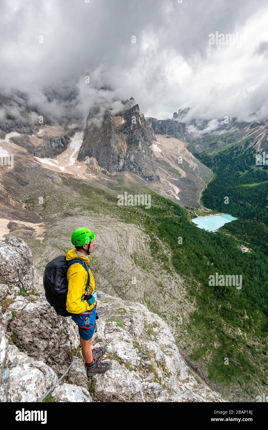 Junger Mann, Bergsteiger auf einer festen Seilstrecke, über Ferrata Vandelli, Blick auf Lago di Sorapis, Sorapiss-Rundkurs, Berge mit niedrigen Wolken, in die Dolden Stockfoto