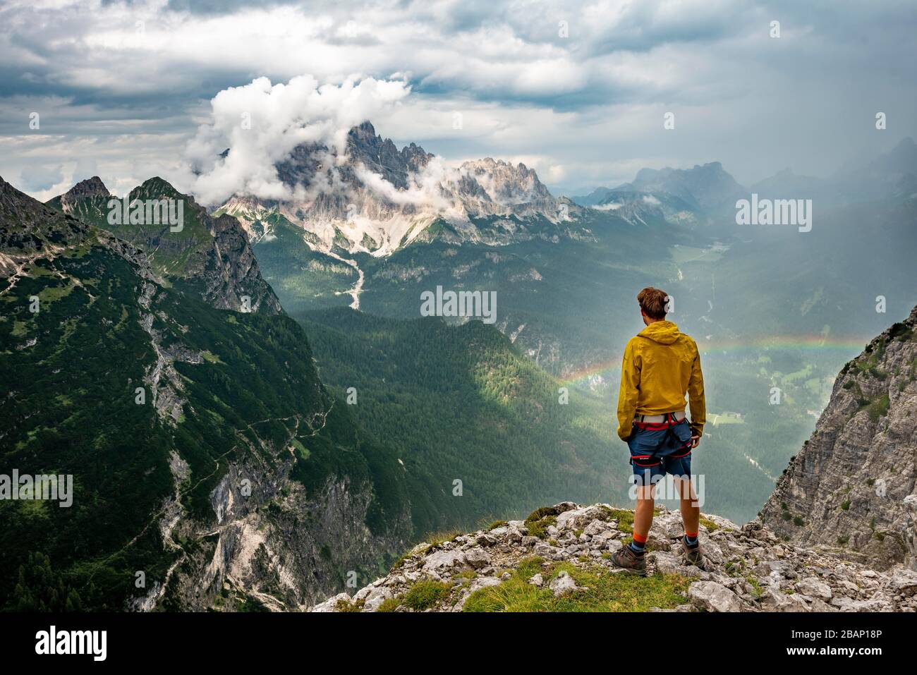 Junger Mann, auf dem Berggipfel Monte Cristallo mit Regenbogen, Wanderer in den Bergen, über Ferrata Vandelli, Sorapiss-Rundkurs, in den Bergen Stockfoto