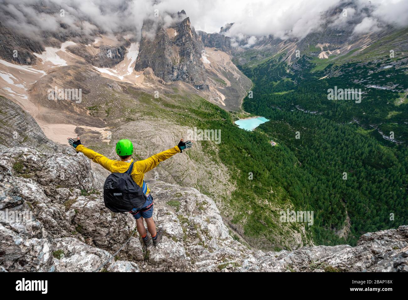 Der junge Mann legt seine Hände in die Luft, kletterer auf einem Klettersteig, über Ferrata Vandelli, Blick auf Lago di Sorapis, Sorapiss-Rundkurs, Berge mit niedrigem Stockfoto