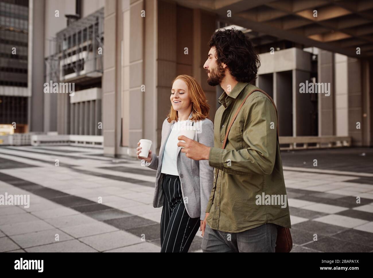 Business man und Frau, die im Freien bei einem Gespräch Kaffee trinken, während sie aus dem Gebäude spazieren Stockfoto