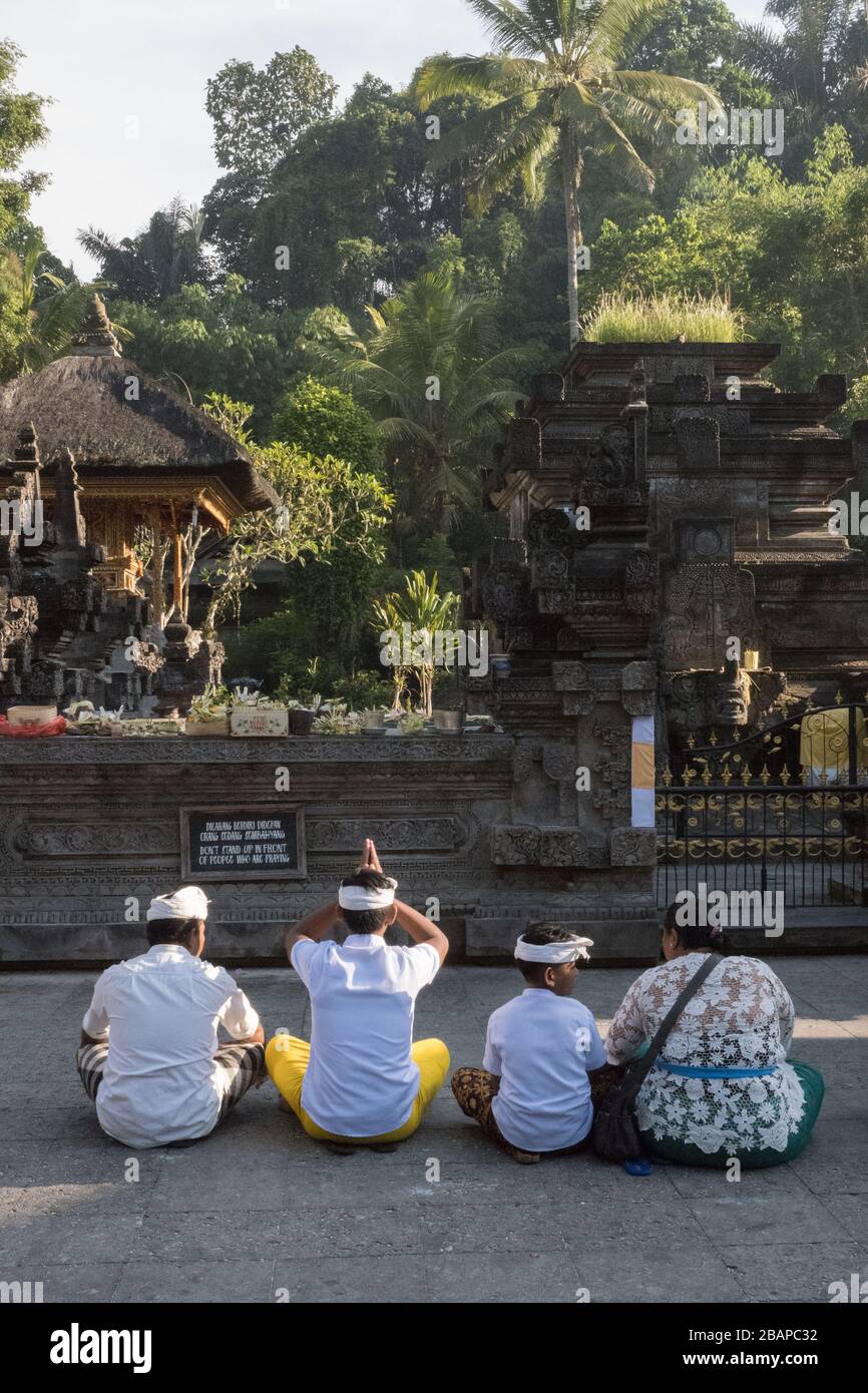 Familie sitzt auf Tempelgelände, mit Blick auf Tempelstatuen, in frühen Morgenstunden Licht beten. Der älteste Sohn hat im Gebet die Hände über dem Kopf zusammengefeilt. Stockfoto