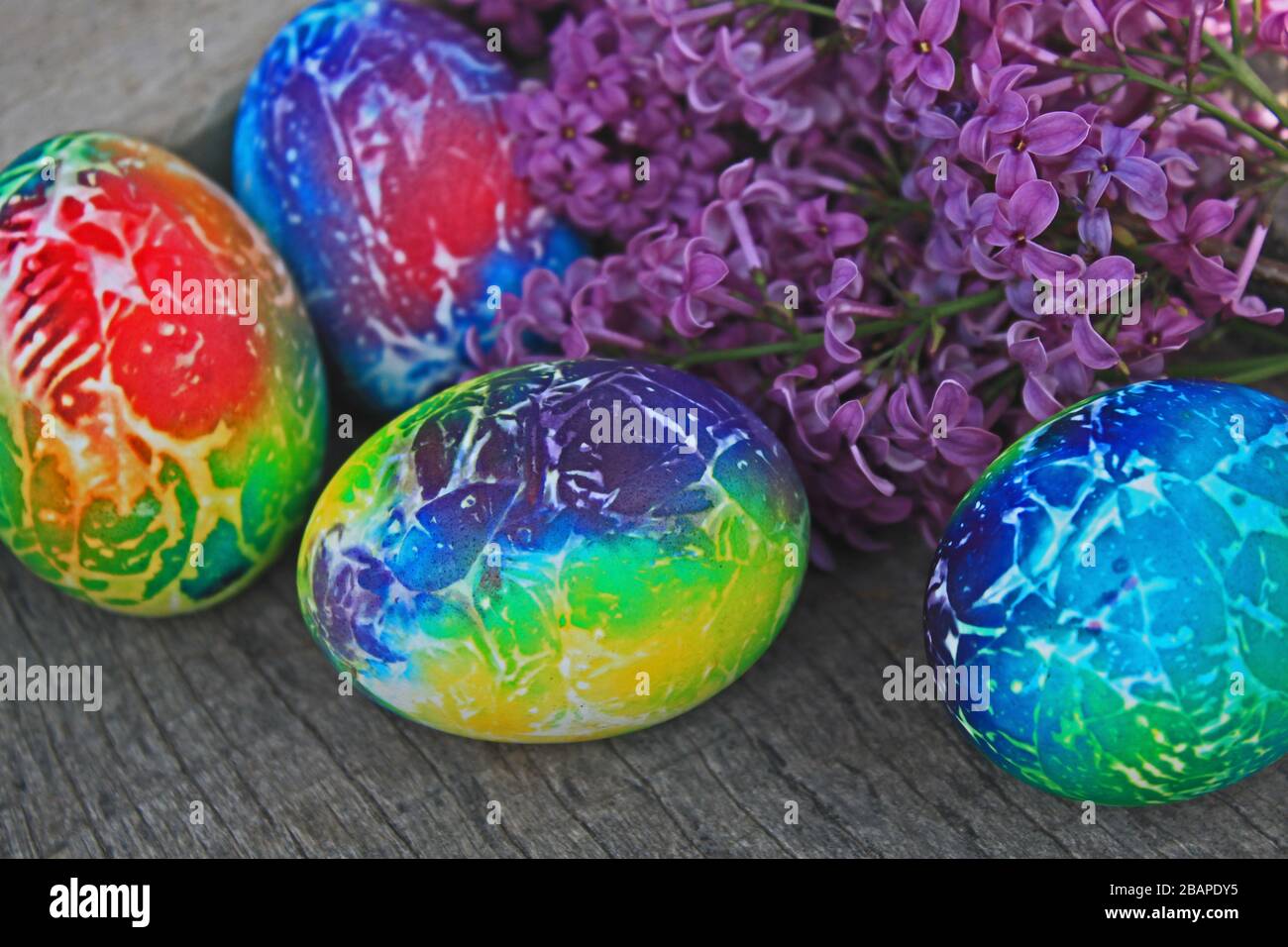 Osterkomposition. Kunstgestaltete Eier mit Flieder auf Holzhintergrund. Stockfoto