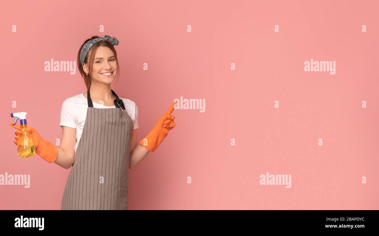 Lächelnde Frau in der Schürze, die Sprayer hält und auf den Kopierbereich zeigt Stockfoto