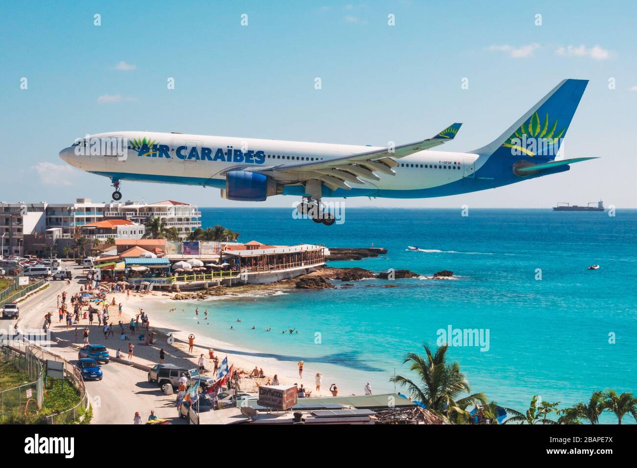 Ein Airbus A330-200 der Air Caraibes-Serie wirft einen Schatten auf Touristen am Maho Beach in St. Maarten Stockfoto