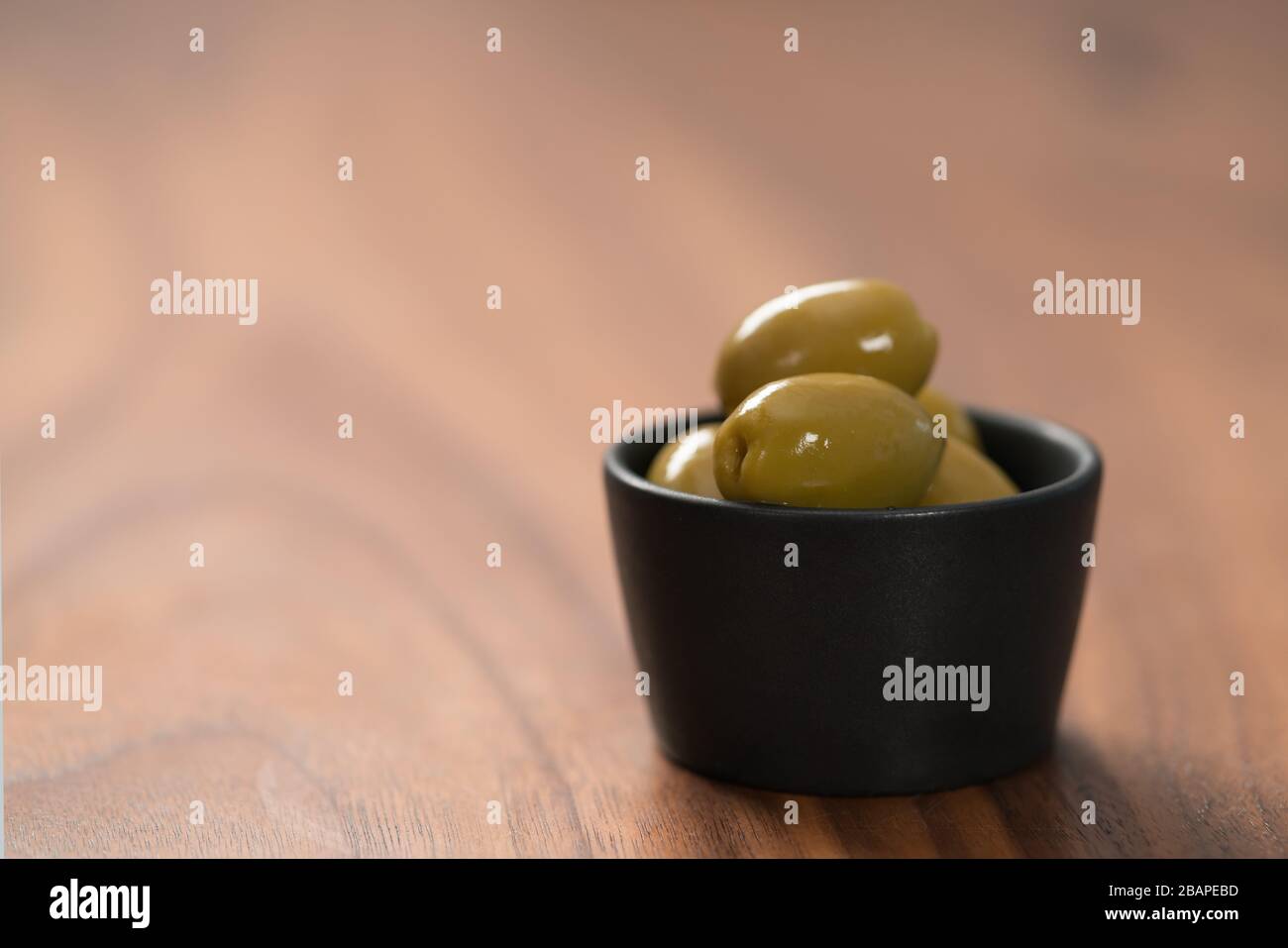 Riesige grüne Oliven in schwarzer Schüssel auf Walnusstisch, flacher Fokus Stockfoto
