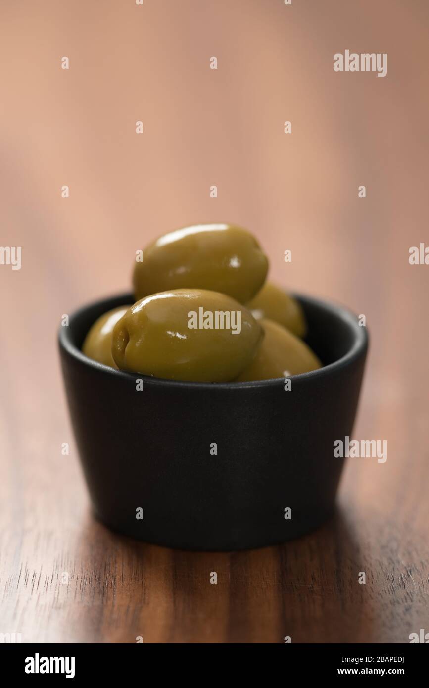 Riesige grüne Oliven in schwarzer Schale auf Walnusstisch Stockfoto