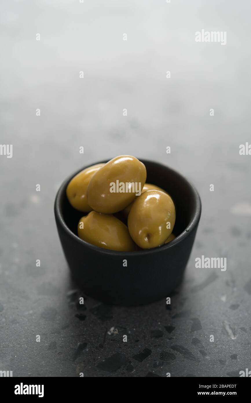 Riesige grüne Oliven in schwarzer Schale auf Betonoberfläche Stockfoto