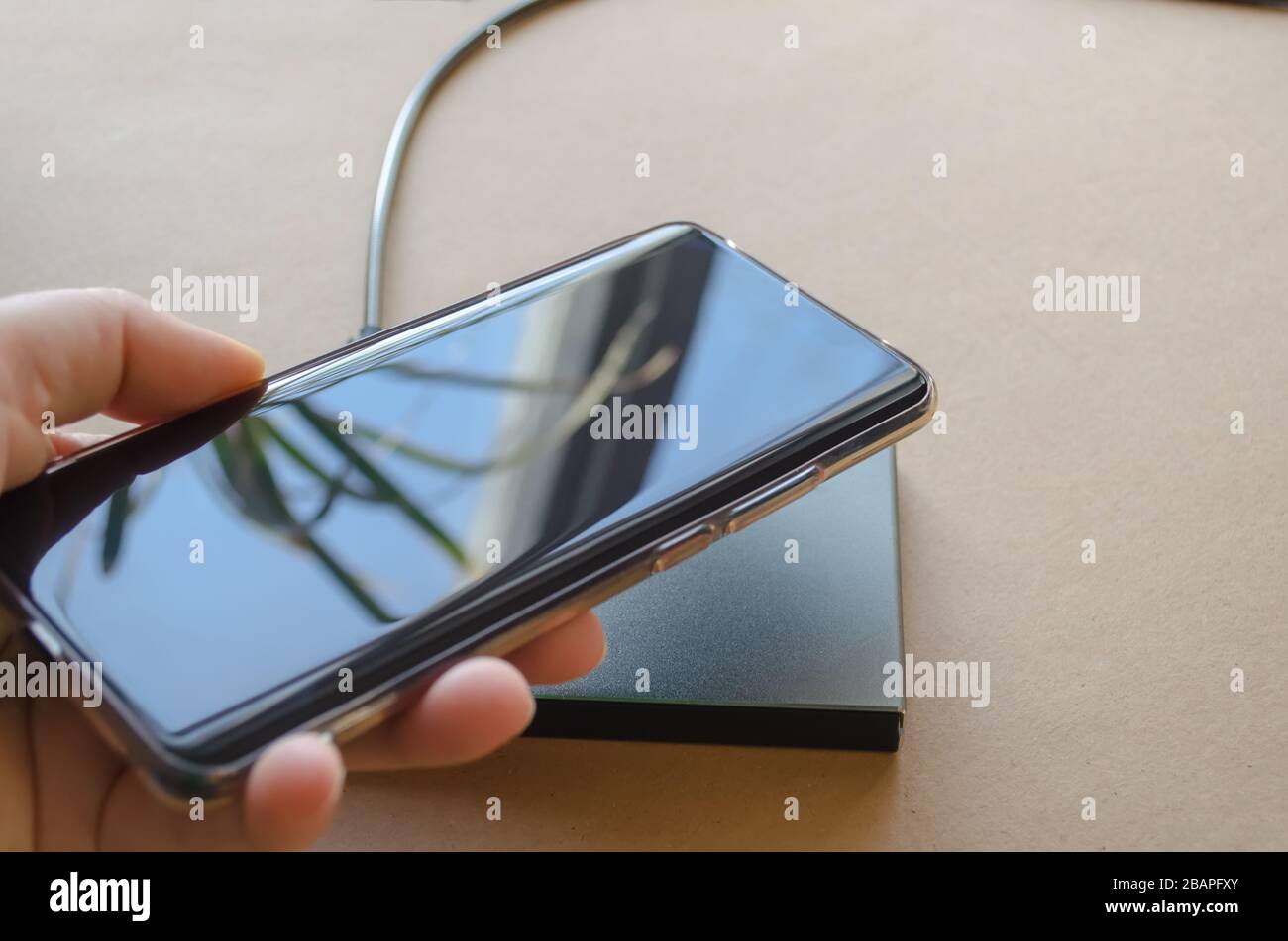 Weibliche Hand bringt das Telefon zum kabellosen Ladegerät. Kabelloses Ladegerät Stockfoto