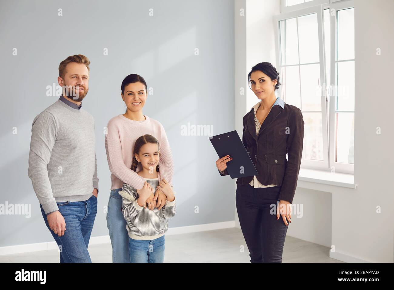 Immobilienmaklerin Frau lächelt mit Zwischenablage und Familie in neuem Zuhause Stockfoto