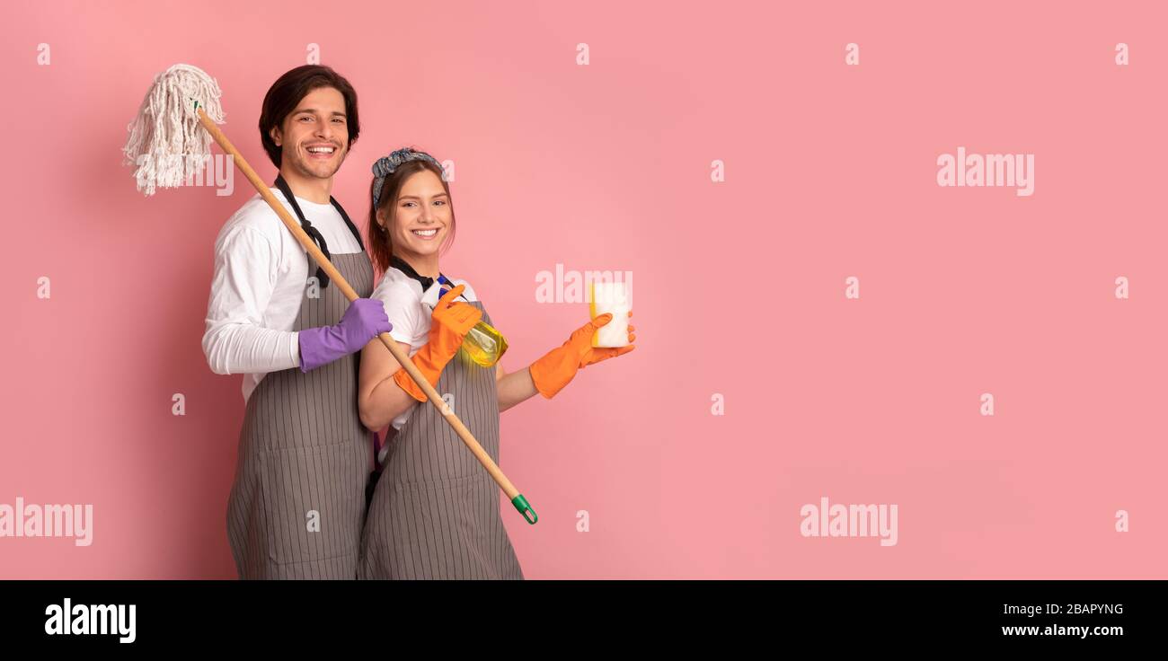 Fröhliche Hausherren Paaren Sich Auf Aprons Mit Reinigungsmitteln Auf Pinkem Hintergrund Stockfoto