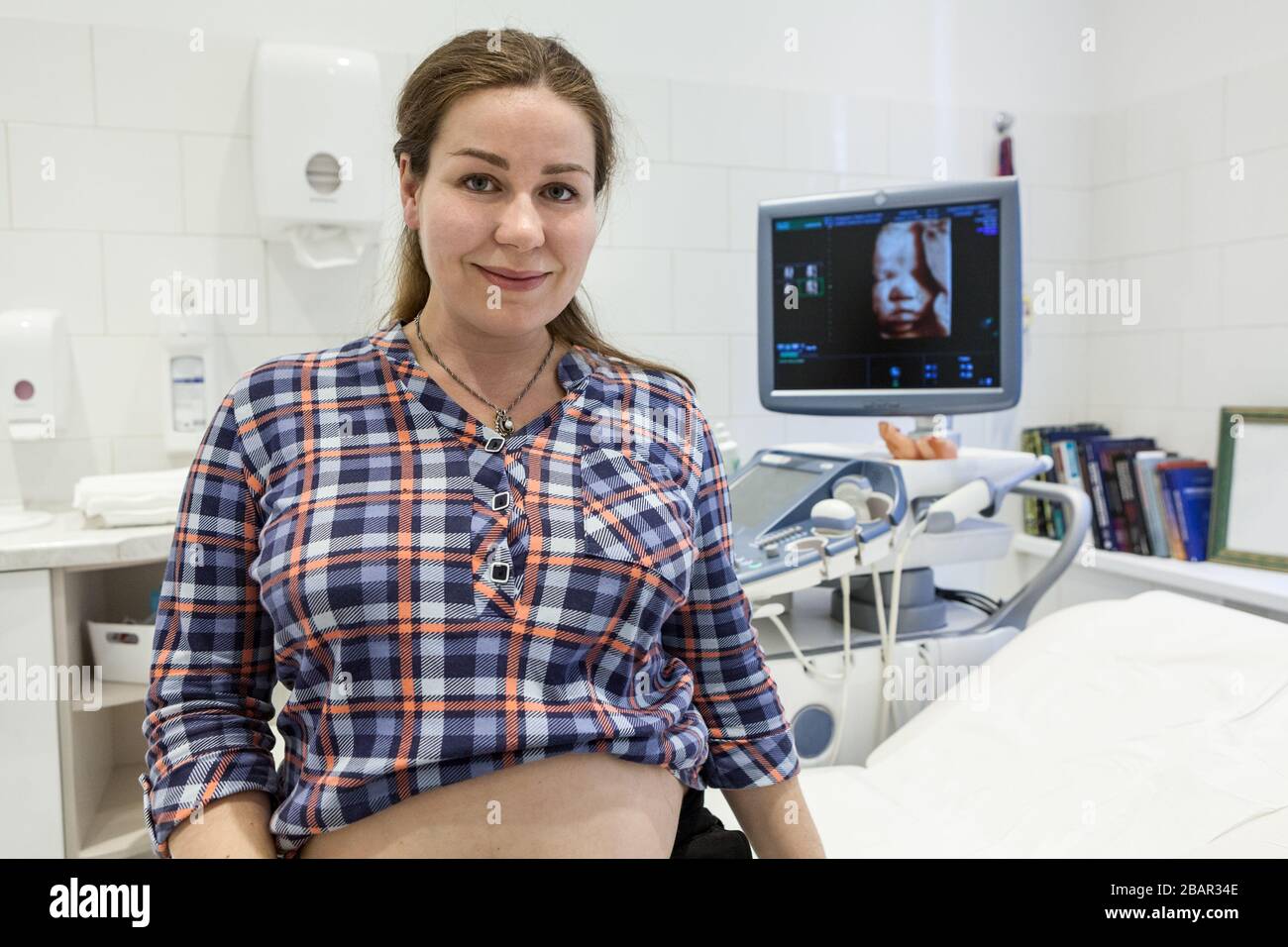 Porträt der schwangeren Frau in einem Krankenhauszimmer mit 3D-Modell des Fötus auf dem Bildschirm des Ultraschallgeräts Stockfoto