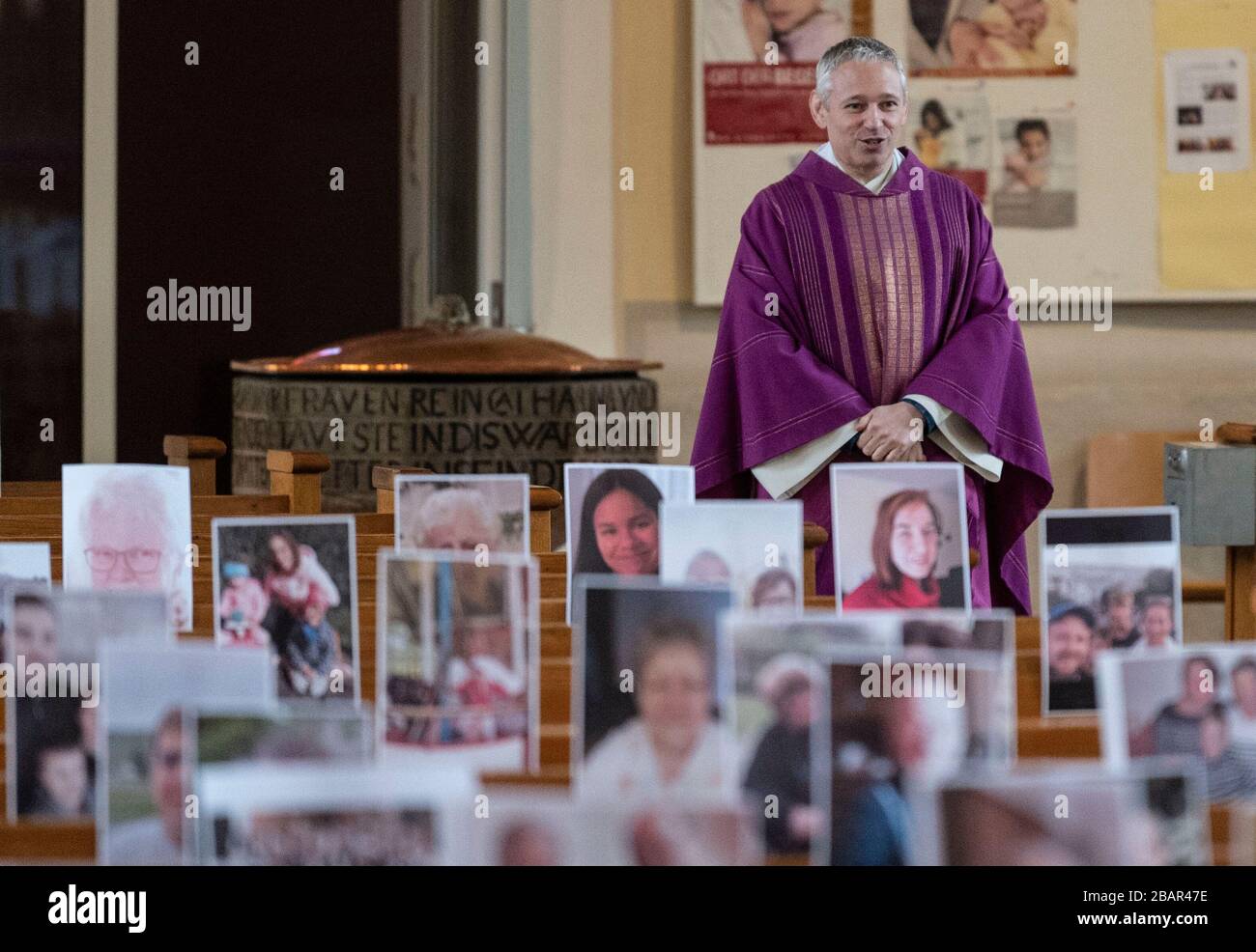 Achern, Deutschland. März 2020. Pfarrer Joachim Giesler steht vor Fotos mit Gemeindemitgliedern in der Pfarrkirche. Gottesdienste finden wegen des Coronavirus vor leeren Kirchen statt. Die Pfarrei hatte ihre Gemeindemitglieder gebeten, Bilder zu senden. Mehr als 300 Bilder wurden ausgedruckt und an den Kirchenbänken aufgehängt. Credit: Patrick Seeger / dpa / Alamy Live News Stockfoto