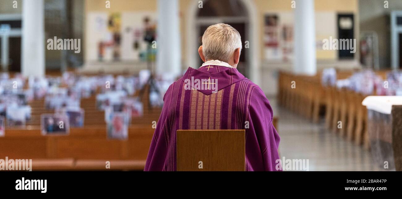 Achern, Deutschland. März 2020. Pfarrer Joachim Giesler sitzt in der Pfarrkirche vor Fotos mit Gemeindemitgliedern. Gottesdienste finden wegen des Coronavirus vor leeren Kirchen statt. Die Pfarrei hatte ihre Gemeindemitglieder gebeten, Bilder zu senden. Mehr als 300 Bilder wurden ausgedruckt und an den Kirchenbänken aufgehängt. Credit: Patrick Seeger / dpa / Alamy Live News Stockfoto