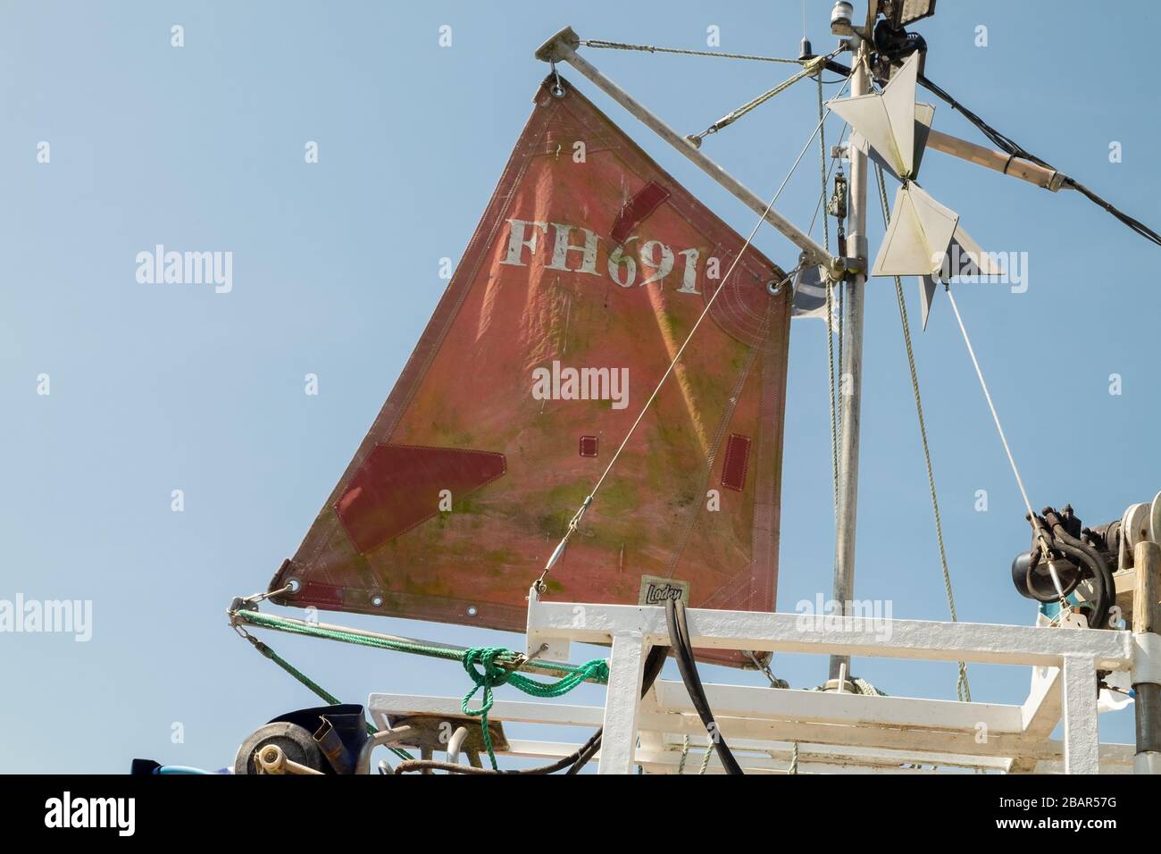 Kleines schmutziges Rot gepatcht, repariertes Segel und Mast auf traditionellem Fischerboot in dem kleinen Fischerdorf Cadgwith, Cornwall, England, Großbritannien. Stockfoto