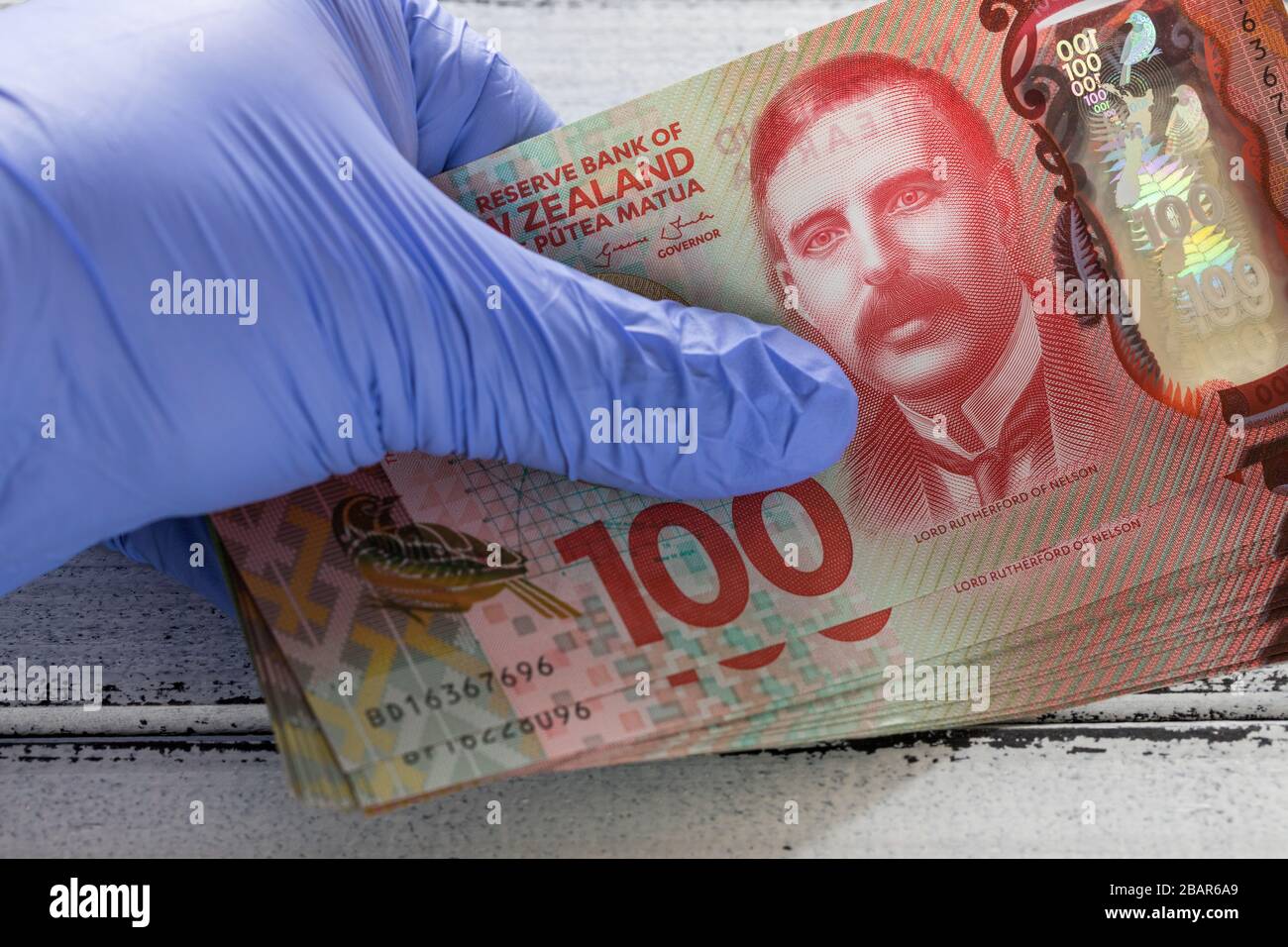 Neuseeländische Dollar, 100 Dollar Banknoten in Gummihandschuhen. Das Konzept der Wirtschaft und der finanziellen Bedrohungen während der Coronavirus Pandemie Stockfoto
