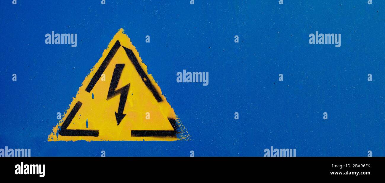 Warnschild. Stromgefährdungsschild an einer blauen Wand mit Farbtropfen und Splatter. Horizontale Aufnahme mit Kopierbereich. Stockfoto