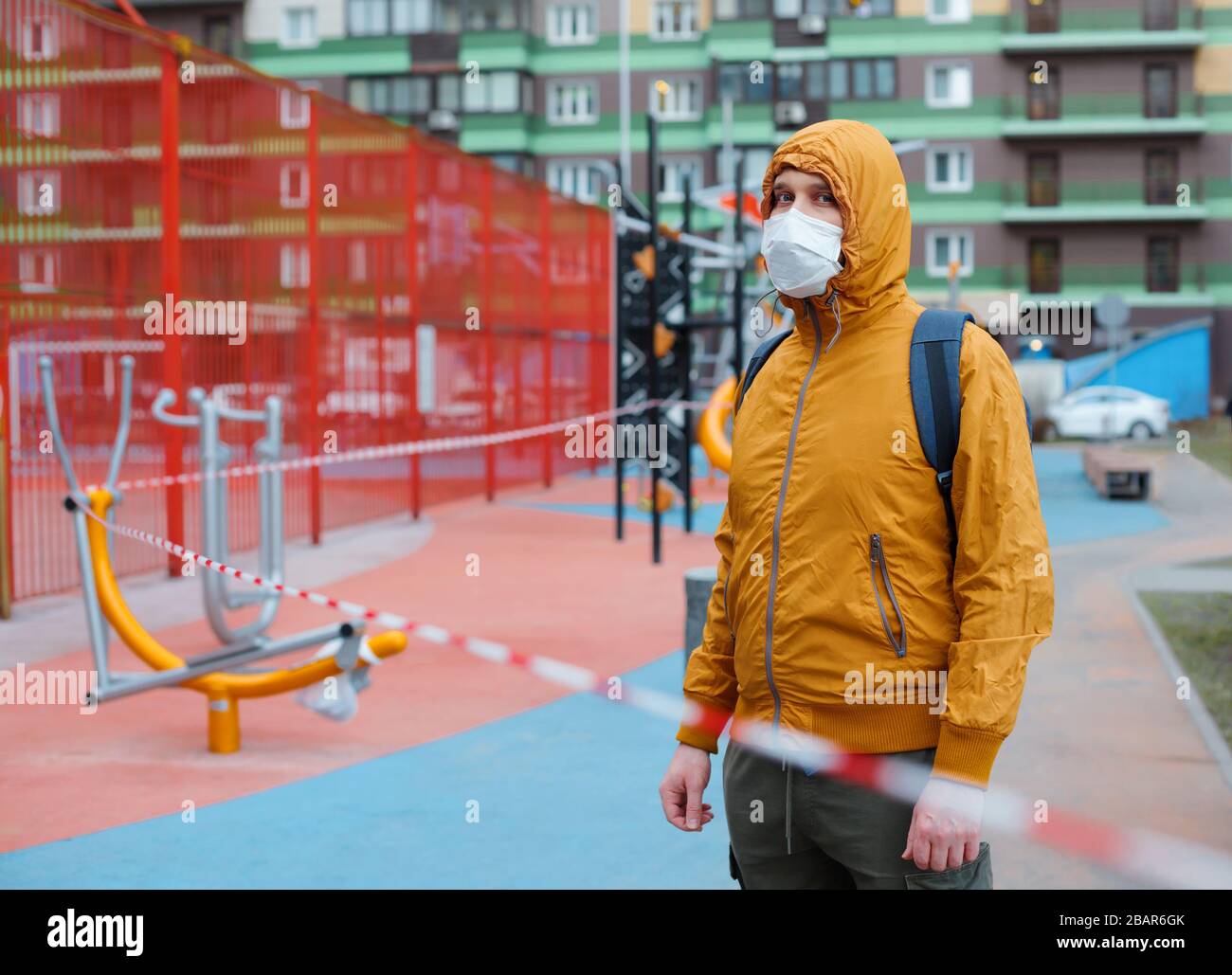 Weißer Mann in Schutzmaske hinter Band eingezäuntem Outdoor-Fitnessstudio. Quarantänebeschränkungen für Covid 19. Stockfoto