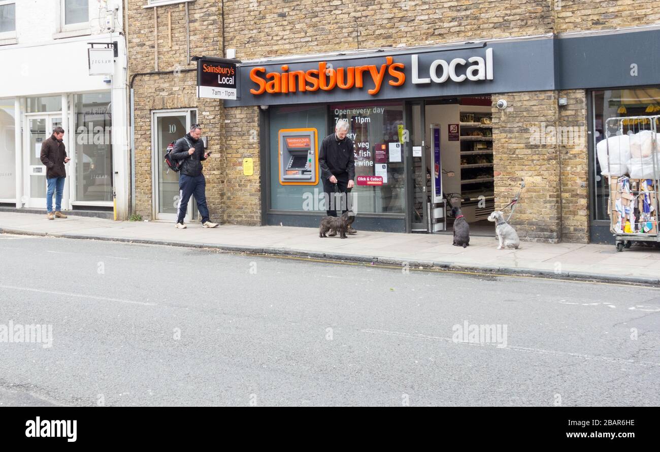 London, England, Großbritannien. März 2020. Käufer, die soziale Distanzierung außerhalb eines lokalen Supermarktes von Sainsbury in der Barnes High Street, London, Großbritannien, Unternehmen Stockfoto