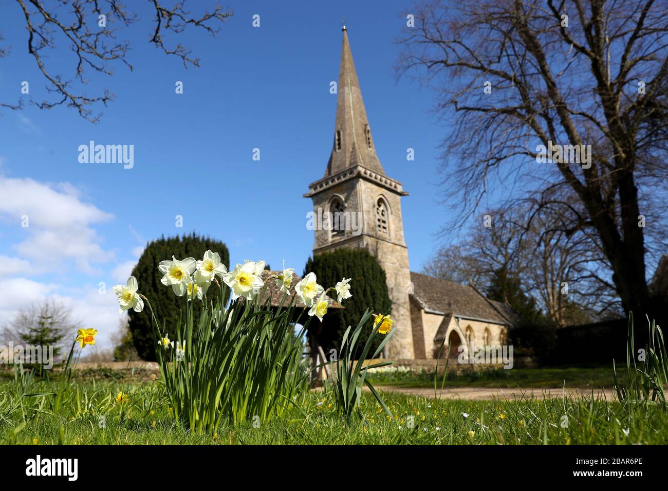 Narzissen, die außerhalb der Parish Church of Saint Mary im Dorf Lower Slaughter in den Cotswolds, Gloucestershire wachsen, während die Uhren eine Stunde in die britische Sommerzeit (BST) vorrücken. Stockfoto