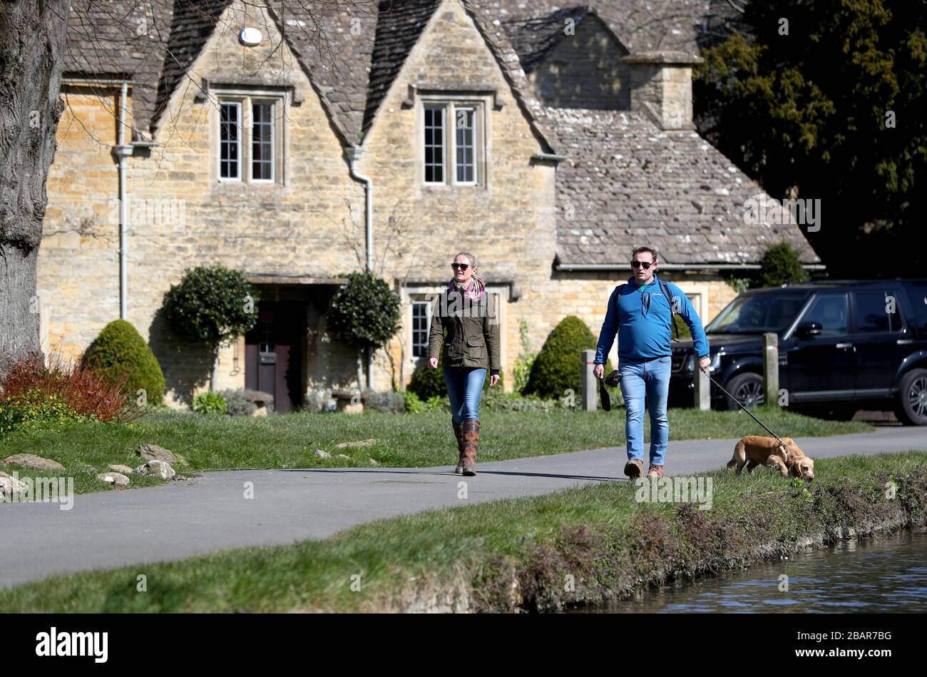 Hundegänger im Dorf Lower Slaughter in den Cotswolds, Gloucestershire, während die Uhren eine Stunde nach British Summer Time (BST) vorrücken. Stockfoto