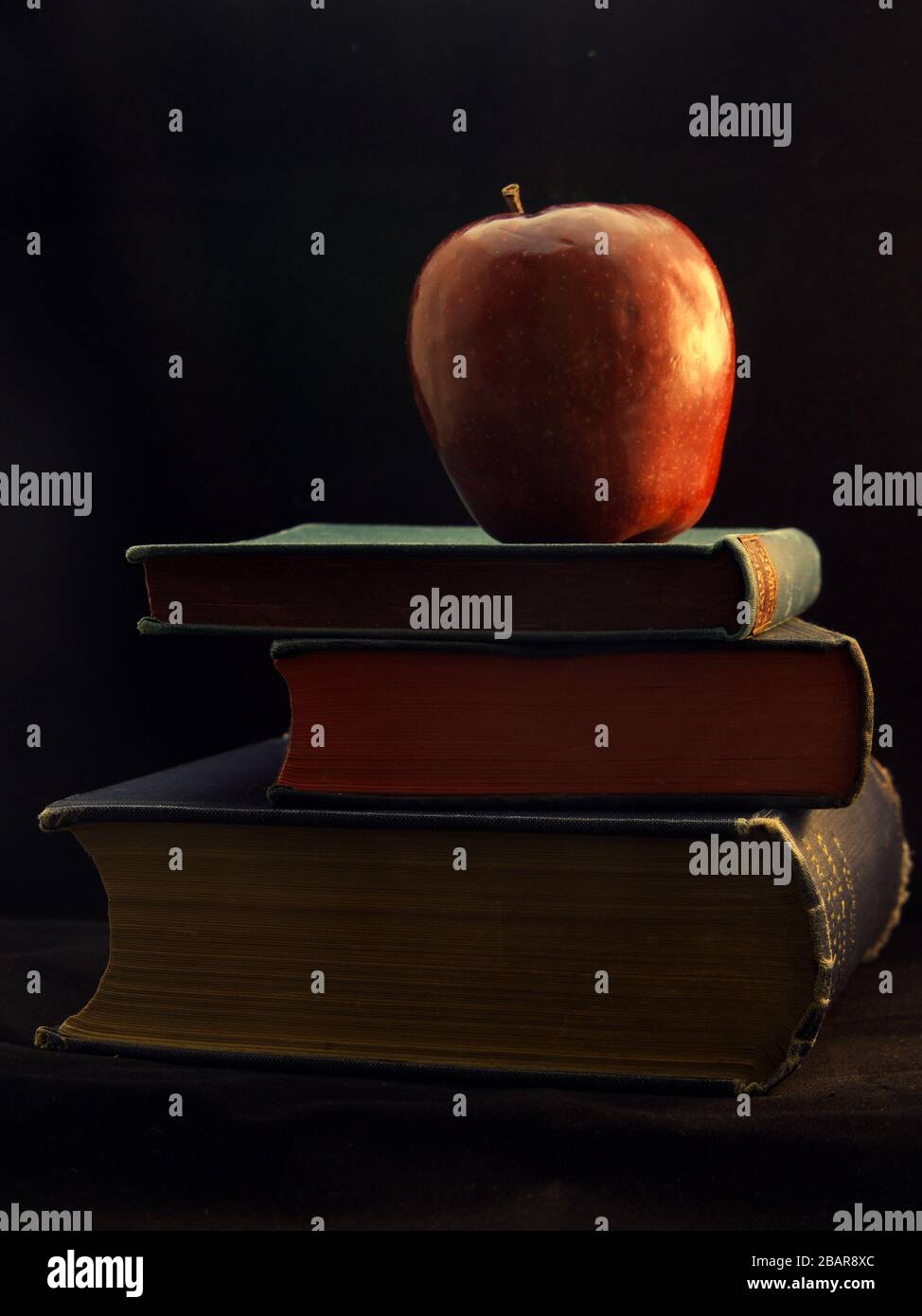 Apple und Bücher im Chiaroscuro-Stil, was den Effekt der Lichtmodellierung in der Fotografie darstellt Stockfoto