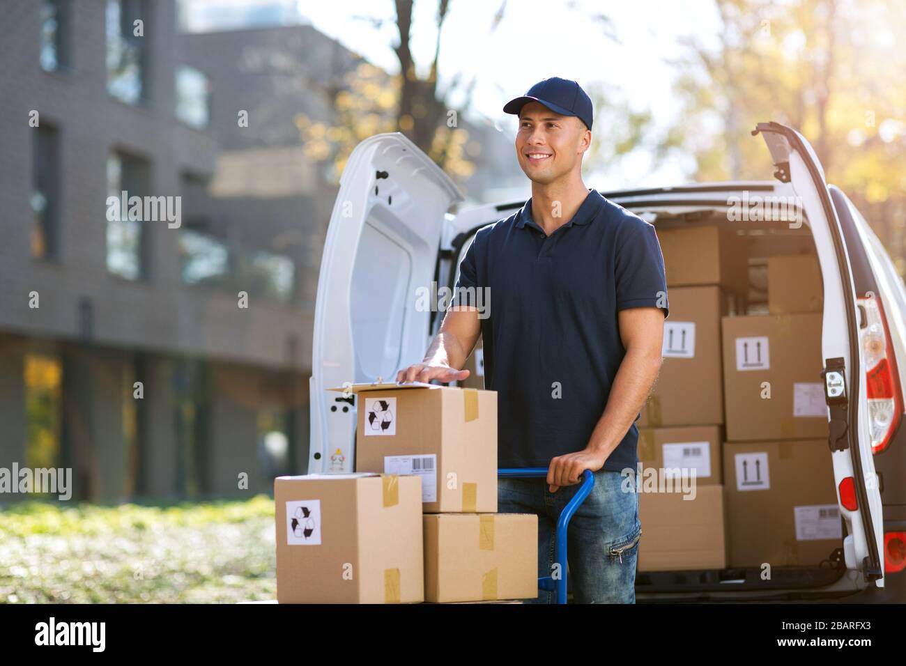 Lächelnder Liefermann mit seinem Lieferwagen Stockfoto