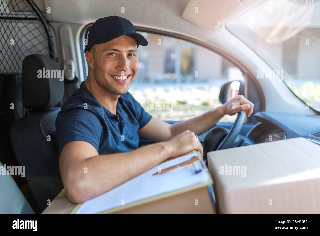 Lächelnder Liefermann mit seinem Lieferwagen Stockfoto