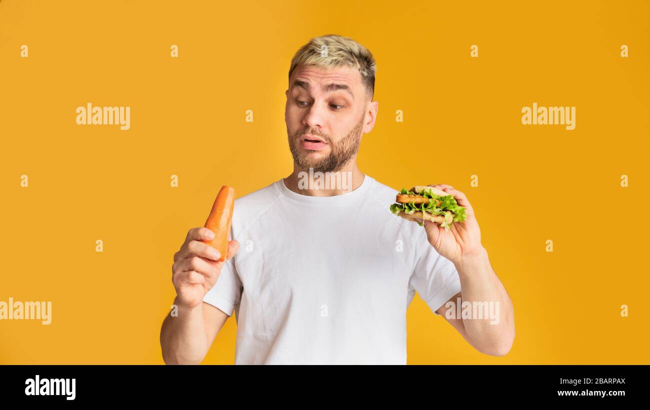 Der lächerliche Mann wählt Gemüse oder fast Food Stockfoto