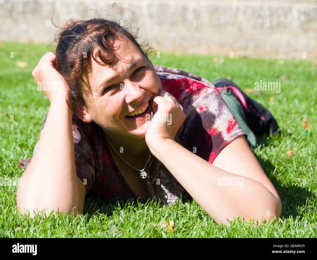 Frau mittleren Alters, die bei Sonnenschein auf dem Gras liegt, Großbritannien Stockfoto