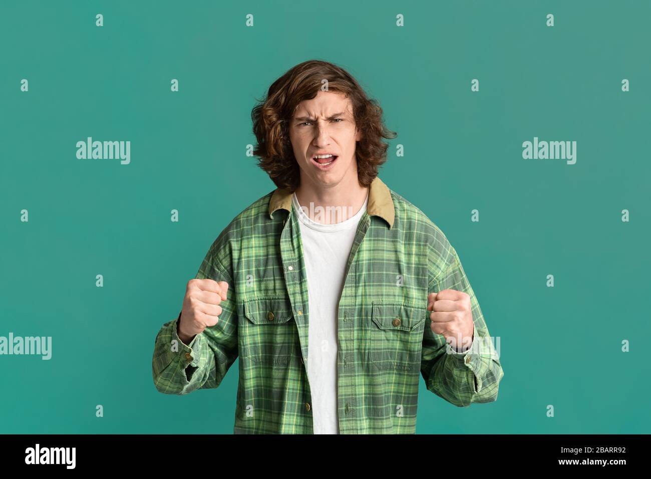 Konfliktkonzept. Gestresster, tausendjähriger Kerl, der Fäuste auf dem Farbhintergrund klungen Stockfoto