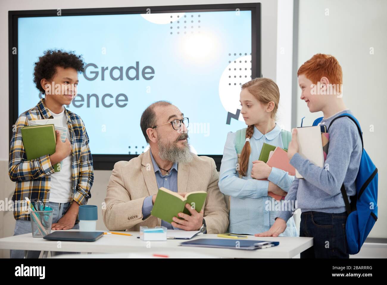 Multiethnische Gruppe von Kindern, die im Schulunterricht um bärtige Lehrer herum stehen, Kopierraum Stockfoto