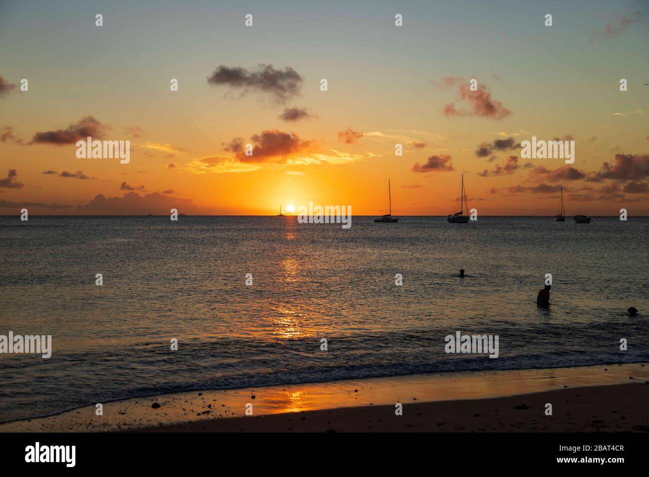 Wunderschöner oranger und gelber Sonnenuntergang, die Horizont-Linie und der Himmel wenige Wolken, die Reflexion der Sonne an Meer und Ufer, Menschen im Meer mit Jachten und Booten Stockfoto