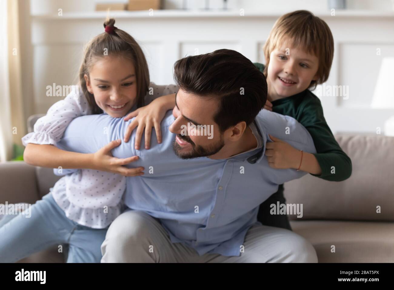 Verspielter junger Papa, der Spaß mit energiegeladenen kleinen Kindern hat. Stockfoto