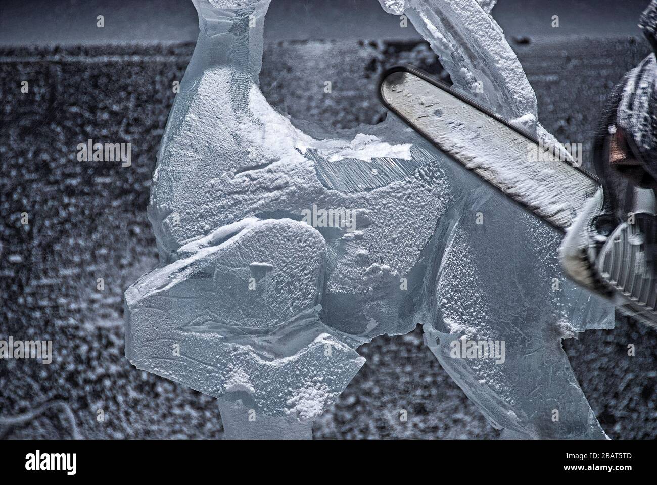 Eiskunstkulptor-Schnitzer mit einer Kettensäge, um einen gefrorenen Eisblock in ein Bild eines Rentiers zu schnitzen Stockfoto